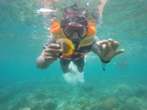 Man snorkeling in clear turquoise water near Tulum, gently holding a small tropical fish underwater.