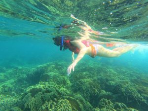 Snorkeler floating above coral reef in clear turquoise water near Tulum, Mexico.